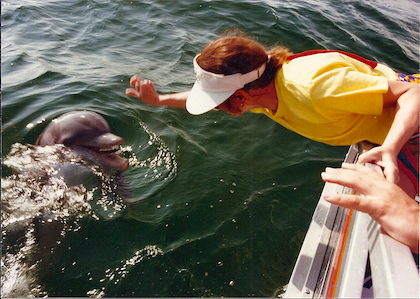 picture of Barbara feeding a fish to a dolphin off the side of a party barge.